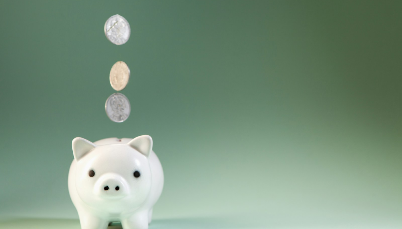 Coins falling into a white piggy bank.