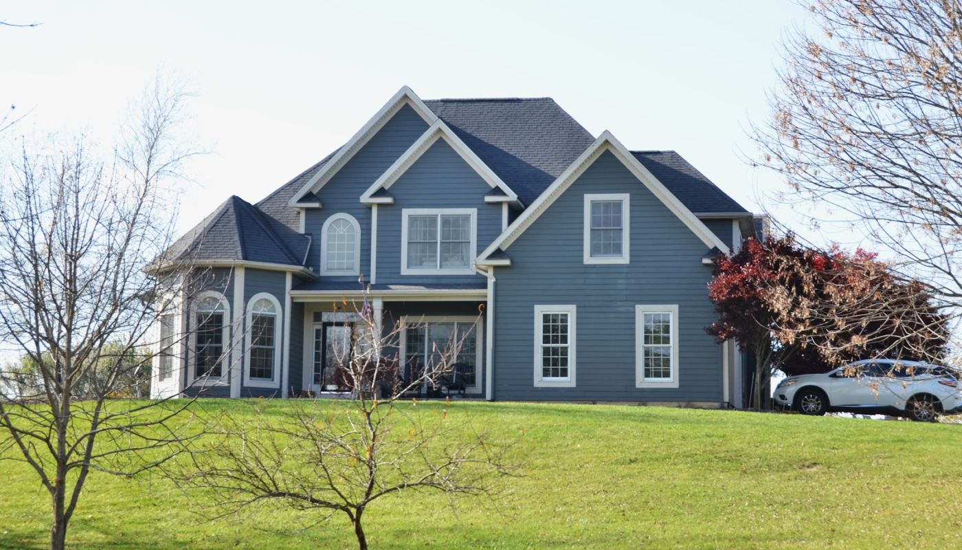 A large blue house sits on a grassy hill.