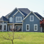 A large blue house sits on a grassy hill.